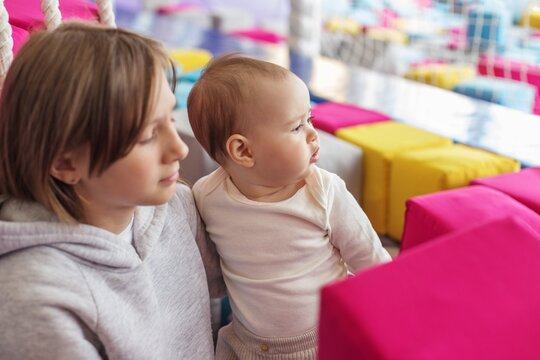 Older sister holding baby at indoor playground. Family time