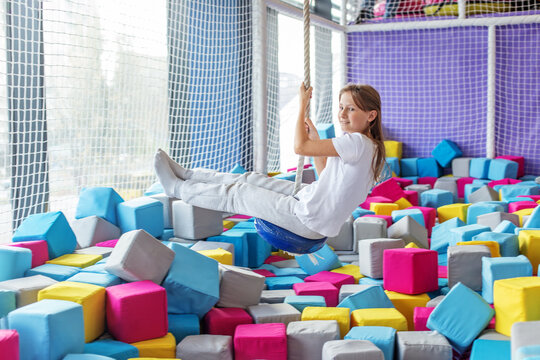 Girl swinging on rope over foam pit in indoor playground