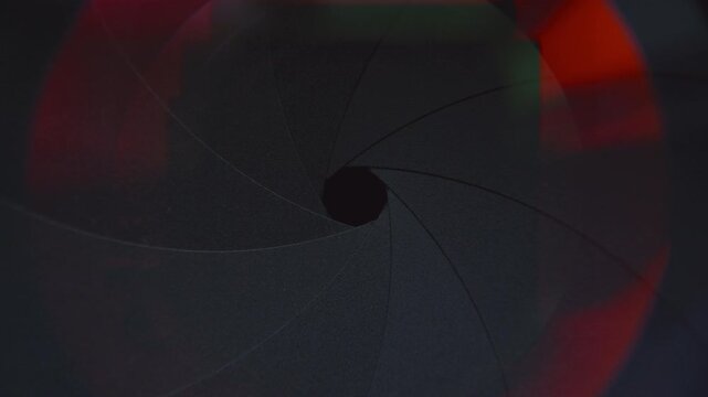 Extreme close-up shot of symmetrical aperture blades closing and forming small central opening in camera lens with colorful light reflections