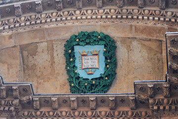 The iconic University of Oxford coat of arms carved into an old stone building. The shield shows an open book and three crowns, with the latin motto.