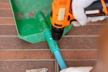 Close-up hand of man to repair the plastic dustpan with using a cordless drill hole a plastic PVC pipe.