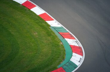 Fototapeta premium Aerial photo of race track corner. Red and white curb marks edge. Green grass separates asphalt and safety feature. Motorsports, speed theme.