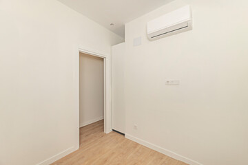 Image of an empty studio with low partitions, featuring small white built-in wardrobes recessed into a custom-built niche, with handles flush with the edge of the doors