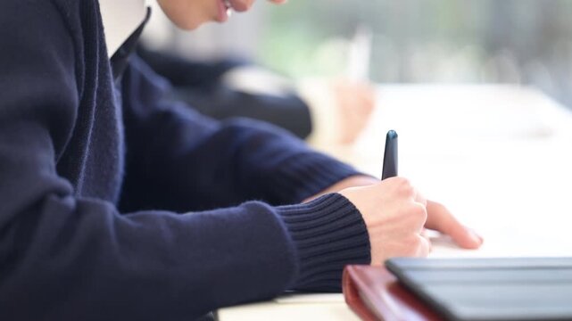 Close-up video of a high school student's hands writing in a notebook during class at school or cram school lessons. No face shown.