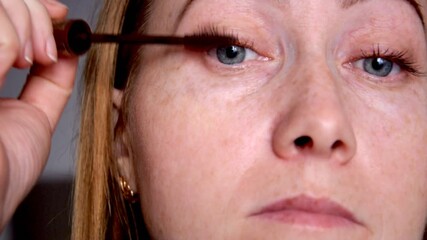Woman applying brown mascara to eyelashes close up
