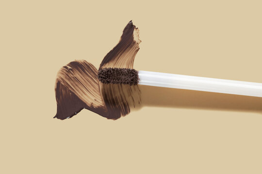 Professional brown brow mascara swipe with applicator brush on neutral beige background. Perfect cosmetic swatch for beauty blogging, modern makeup design, or minimalist fashion advertisement