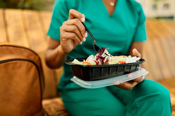 Young woman or a nurse or a doctor during office hours break enjoying a fresh salad in a park during a sunny day while smiling and relaxing on a bench