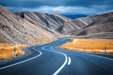A beautiful winding asphalt road leads through a vast, dry mountain landscape under a dramatic cloudy sky, inviting adventure and scenic exploration.
