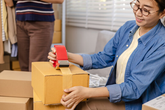 Small business warehouse store, women workers apply shipping label on parcel and taping cardboard box, organizing delivery tasks, order preparation, inventory management packing workflow, multitasking