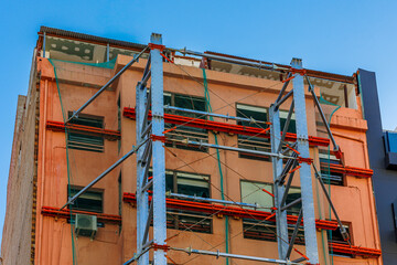 Naklejka premium Building Facade Reinforced with External Steel Structure, Urban building exterior under renovation, featuring external steel framework and scaffolding for structural reinforcement.