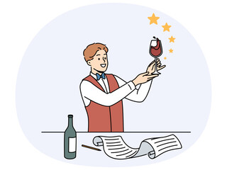 Man sommelier holds glass red wine and evaluates taste of noble alcoholic drink standing near table with bottle and sheet of paper. Guy studying at sommelier school wanting to get job in restaurant