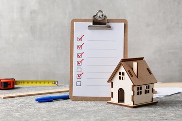 A detailed home inspection checklist positioned next to a miniature house model placed on a workspace desk