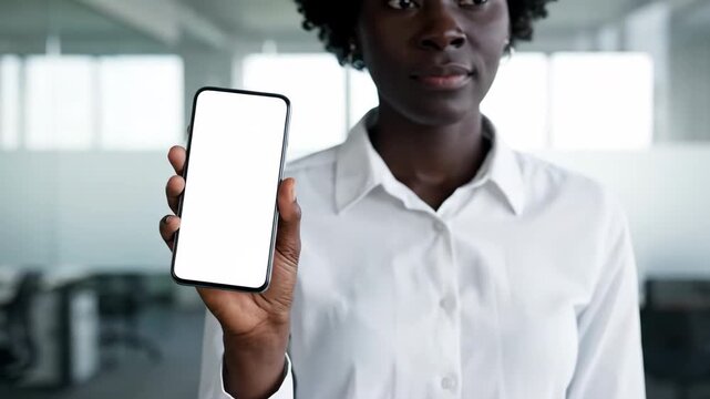 Young woman holds a smartphone with a blank white screen in an office setting.