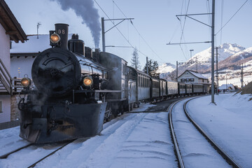 A steam locomotive driving through the Swiss alps in the winter.
