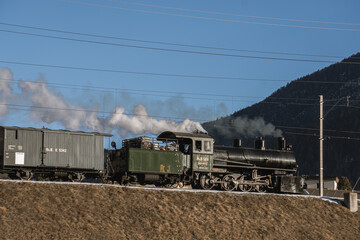 A steam locomotive driving through the Swiss alps in the winter.