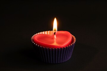 A heart shaped red candle burns brightly on a dark background in a purple wrapper with love and romantic with mood