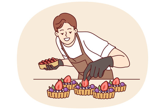 Man confectioner prepares sweet dessert with berries and butter cream for sale in coffee shop or restaurant. Guy in apron stands at kitchen table making delicious dessert for bakery visitors