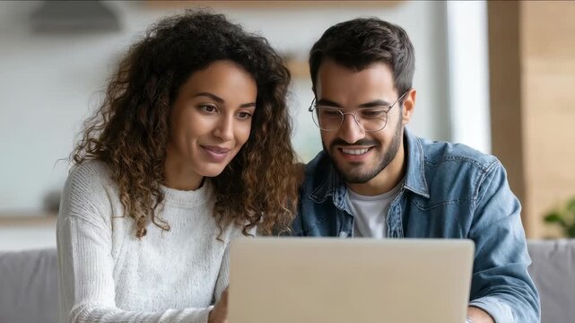 Happy young couple smiling while using a laptop together at home, enjoying a relaxing moment. Modern lifestyle and technology bring people closer and foster positive relationships