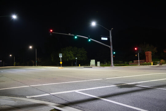 Empty intersection at night in Corona, California, featuring illuminated traffic lights, crosswalk markings, and wide urban roadway.