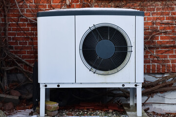 Outdoor heat pump unit standing against brick wall during winter