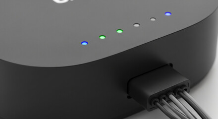 A sleek black electronic device, like a router or hub, with a row of glowing status LED lights and a cable plugged in