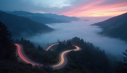 Long exposure photo of winding road at mountain valley during sunrise with foggy weather. Cars light trails on asphalt highway. Scenic landscape with trees and clouds.