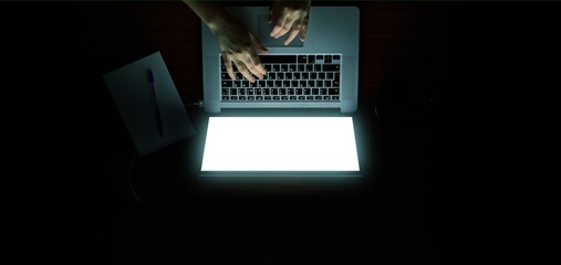 Overhead hacker in the hood working with laptop and mobile phone typing text in the darkroom. Russian hacker hacking the server in the dark.