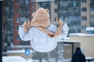 Girl riding on a swing during snow. Relax and leisure in winter city