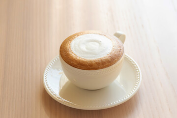 Creamy cappuccino with foam in white cup on saucer on wooden table, warm morning mood