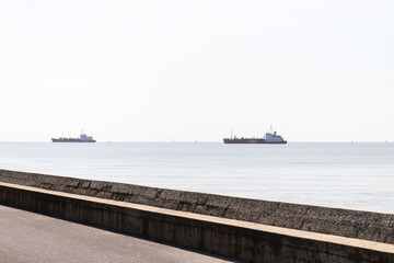 Calm seascape with cargo ships on horizon and stone promenade in foreground conveying serenity