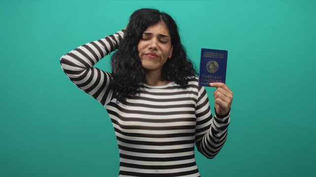 Woman holding belarus passport with hand to head in studio with teal background; travel uncertainty.
