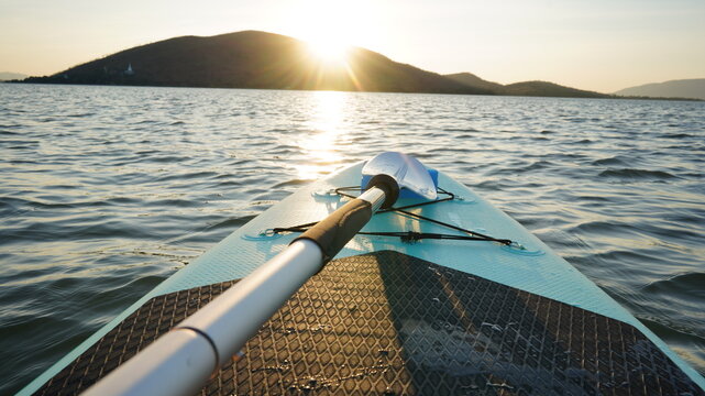 Blue turquoise SUP board in wavy open water. Stand Up Paddle board activity has water sport in the dam during hill in twilight sun. Rowing boat in nature.