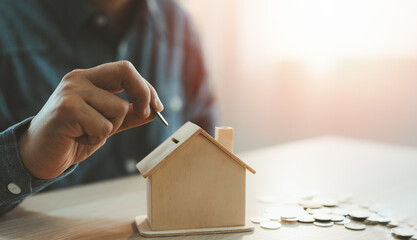 A man hand putting coins into a house bank saving bank for account save money. Planning step up, saving money for future plan, retirement fund. A business investment-finance accounting concept.