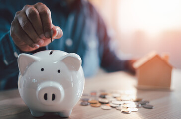 A man hand putting coins into a white piggy bank for account save money. Planning step up, saving money for future plan, retirement fund. A business investment-finance accounting concept.
