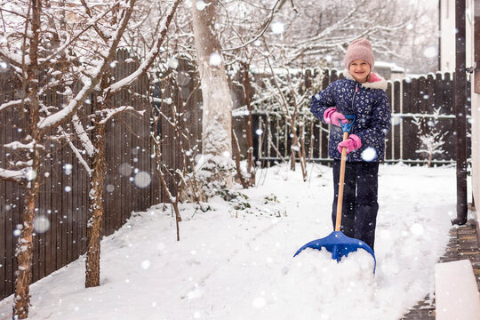 Snow Shovel for Winter Cleaning. Happy Little Child Girl Shoveling Snow near House during Snowfall.