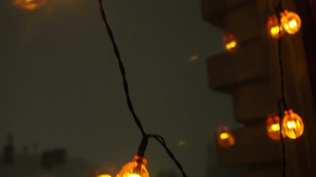 Charming Halloween Garland Displays Glowing Orange Lights Shaped Like Tiny Pumpkins, Perfectly Framed Against Window Glass And The Enchanting Night Sky, Creating A Spooky Yet Delightful Atmosphere.