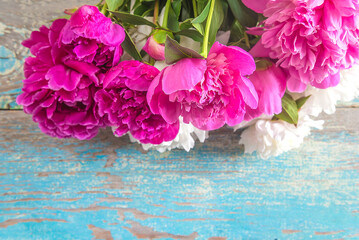 Bunch of purple and pink peony flowers on a old blue paint wooden background; space for text