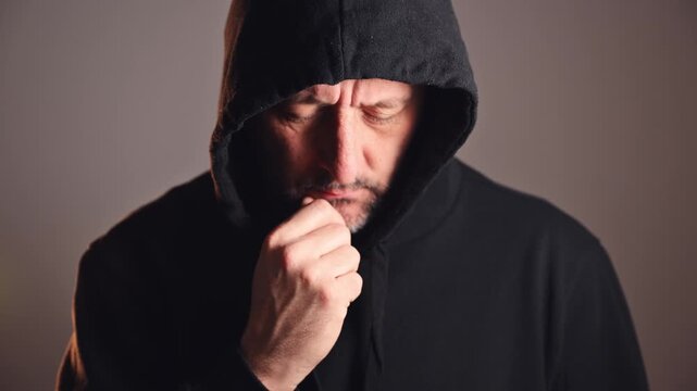 portrait of a middle-aged man with short beard and weathered face, wearing a dark hoodie pulled up, staring directly with furrowed brow and intense gaze. 4K.