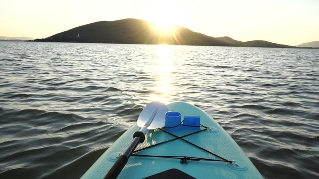 Blue turquoise SUP board in wavy open water. Stand Up Paddle board activity has water sport in the dam during hill in twilight sun. Rowing boat in nature.