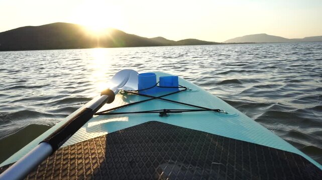 Blue turquoise SUP board in wavy open water. Stand Up Paddle board activity has water sport in the dam during hill in twilight sun. Rowing boat in nature.