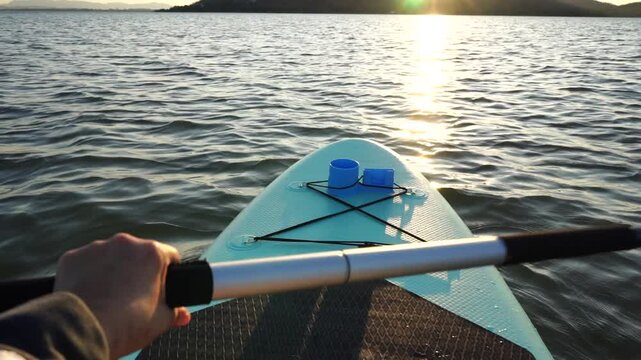 Blue turquoise SUP board in wavy open water. Stand Up Paddle board activity has water sport in the dam during hill in twilight sun. Rowing boat in nature.