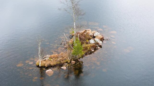 tiny rocky island sits middle calm lake submerged stones visible norway aerials forest overhead drone shot boreal landscape nordic wilderness 
