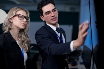 A senior software developer leads a code review session, pointing to a specific function on the screen to explain its logic and syntax to a junior engineer before a major deployment.
