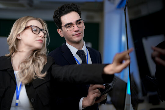 A senior software developer leads a code review session, pointing to a specific function on the screen to explain its logic and syntax to a junior engineer before a major deployment.