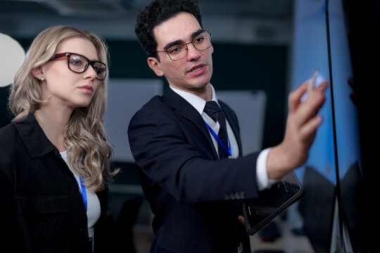 A senior software developer leads a code review session, pointing to a specific function on the screen to explain its logic and syntax to a junior engineer before a major deployment.