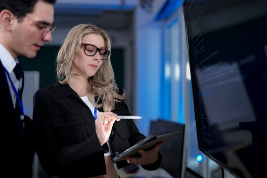 A senior software developer leads a code review session, pointing to a specific function on the screen to explain its logic and syntax to a junior engineer before a major deployment.