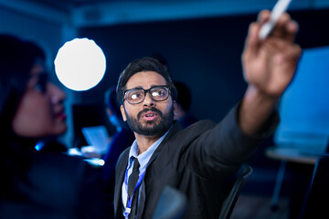 A creative director leads a late-night review session, pointing out key design elements on a large screen to his team, providing artistic direction for a new marketing campaign or UI project.