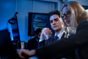 An IT project manager discusses system requirements with her team of software developers and data analysts, reviewing code and performance metrics in a high-tech command center.