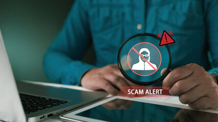 Man holding magnifying glass with virtual Scam Alert icon. Concept of fraud detection, cyber security, hacker protection, online safety, phishing warning and digital crime prevention.