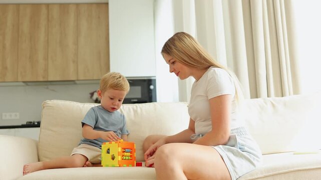 loving mother and small child happily engaged in playtime, using an educational shape sorter toy on the living room sofa. precious family moments and early childhood development in a bright home.